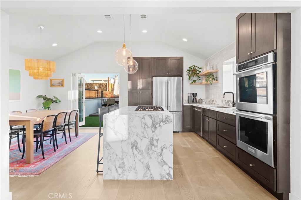 32 56th Place Long Beach, CA 90803 - Photo 5 of 49 a large kitchen with stainless steel appliances kitchen island granite countertop a refrigerator a stove a sink a dining table and chairs with wooden floor