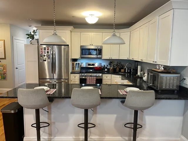 a kitchen with stainless steel appliances granite countertop a refrigerator a stove a sink dishwasher and a chairs with wooden floor