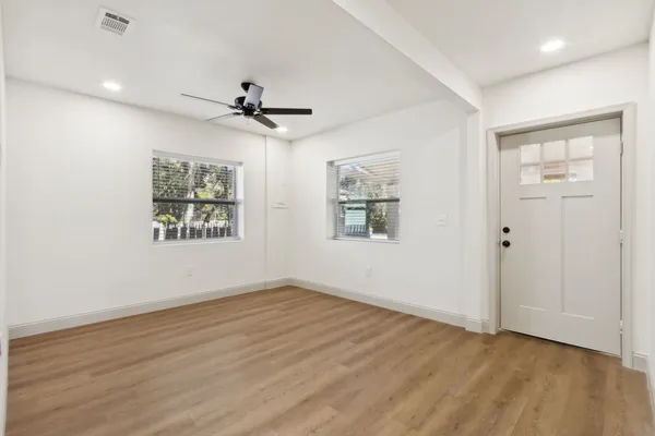 an empty room with wooden floor ceiling fan and windows