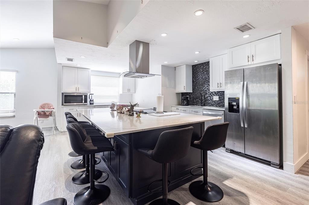 2345 Outrigger Lane Naples, FL 34104 - Photo 10 of 37 a kitchen with stainless steel appliances granite countertop a sink a stove a refrigerator cabinets and a dining table with wooden floor