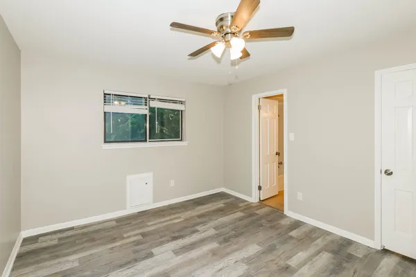 an empty room with wooden floor fan and windows