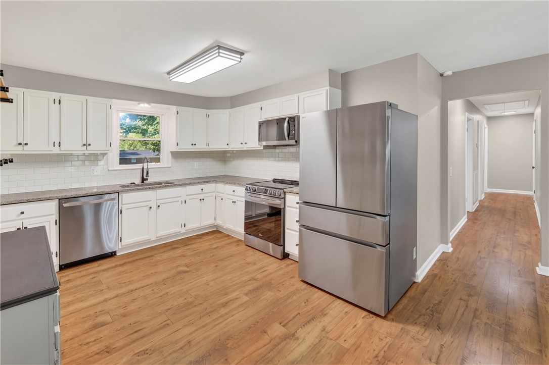 207 Ridgecrest Drive Williamston, SC 29697 - Photo 5 of 22 White cabinetry paired with stainless steel appliances anchors this kitchen with hardwood flooring.