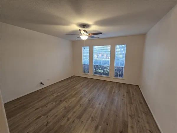 an empty room with wooden floor chandelier fan and windows