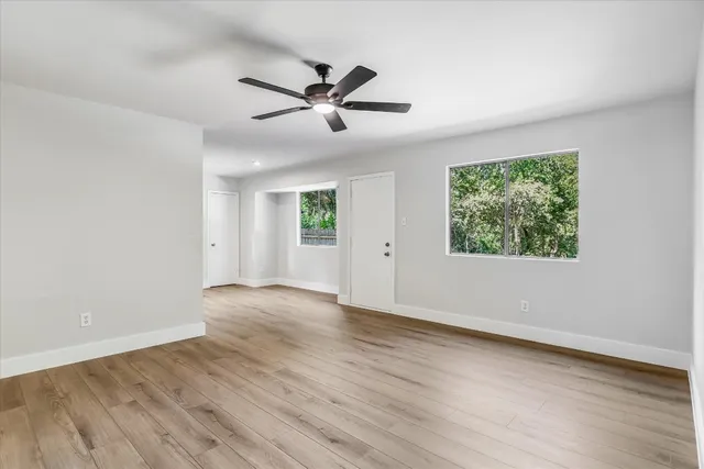 an empty room with wooden floor fan and windows