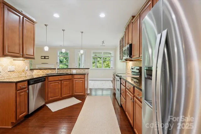 a large kitchen with stainless steel appliances granite countertop a refrigerator a sink dishwasher a stove and a dining table with wooden floor