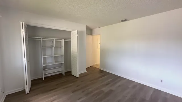 an empty room with wooden floor closet and windows