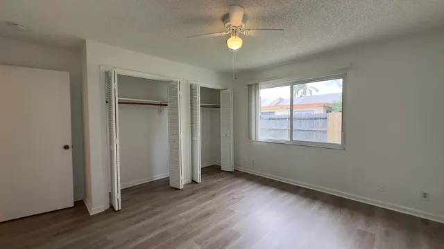 an empty room with wooden floor chandelier fan and windows