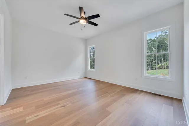 an empty room with wooden floor fan and windows