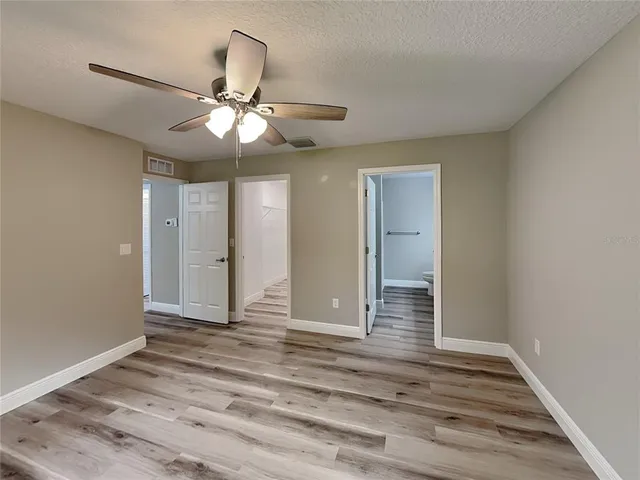 a view of an empty room with wooden floor and a ceiling fan
