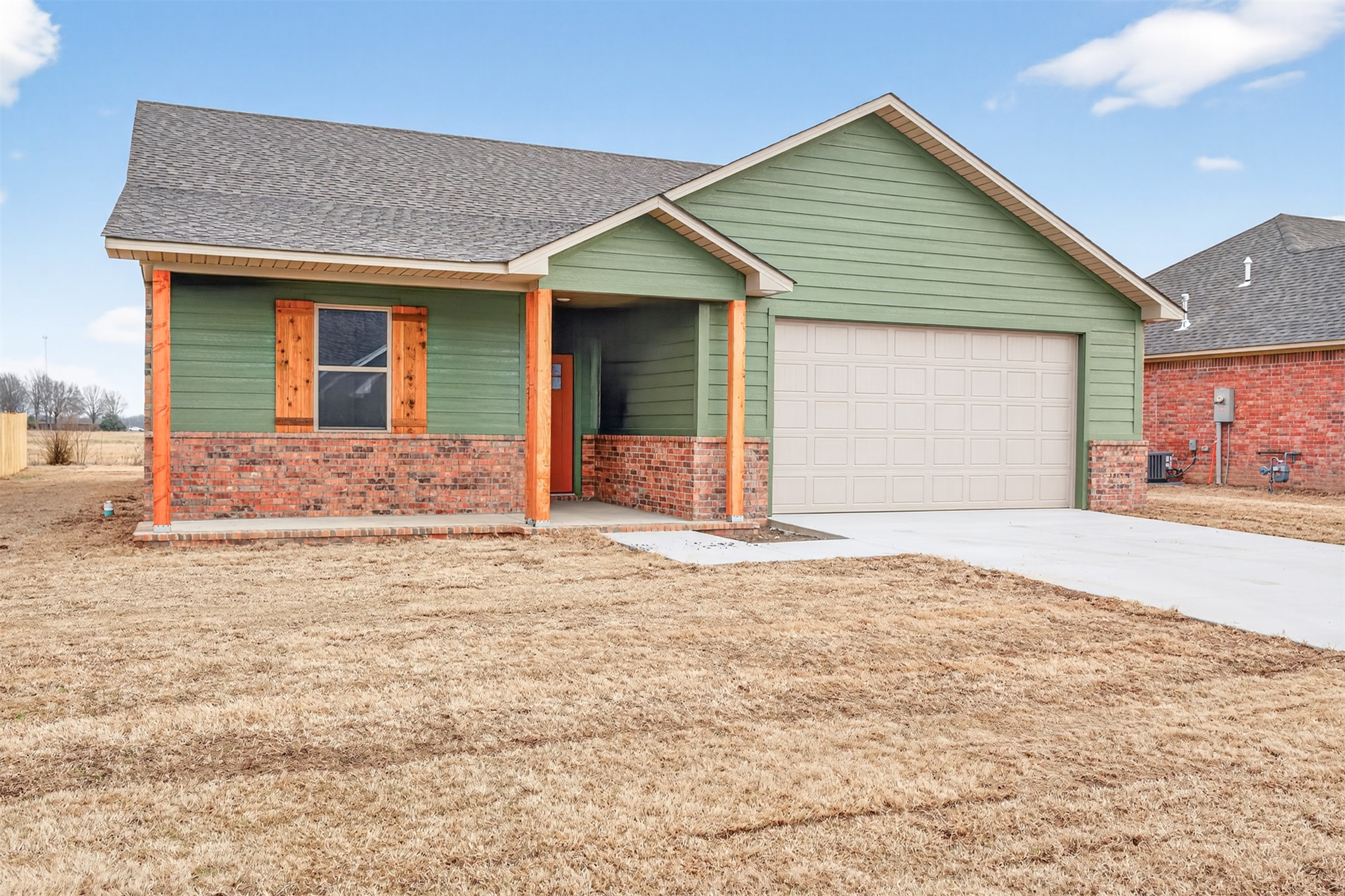 124 Countryside Way Pocola, OK 74902 - Photo 38 of 39 Green siding, brick facade, wood-finish columns, wood-finish shutters, and an attached garage
