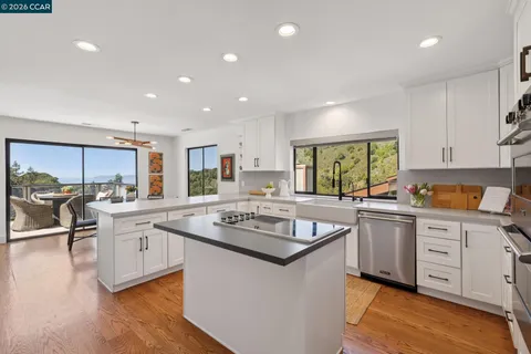 a kitchen with stainless steel appliances granite countertop a stove top oven a sink dishwasher and white cabinets with wooden floor