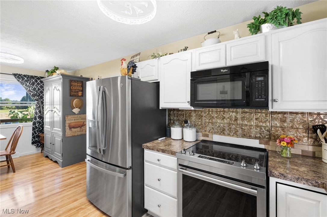 9208 Thorpe Road Berlin Heights, OH 44814 - Photo 8 of 47 Kitchen featuring stainless steel appliances, dark countertops, decorative backsplash, white cabinetry, and light wood-style flooring