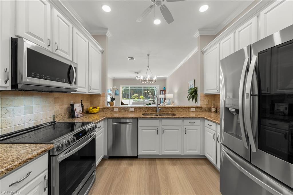 3653 Periwinkle Way, Unit 127 Naples, FL 34114 - Photo 3 of 44 a kitchen with stainless steel appliances granite countertop a stove top oven a sink dishwasher a refrigerator and a microwave oven with wooden floor
