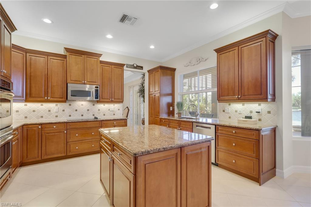 1859 Ivory Cane Point Naples, FL 34119 - Photo 13 of 50 Kitchen with backsplash, brown cabinetry, light stone countertops, stainless steel appliances, and ornamental molding