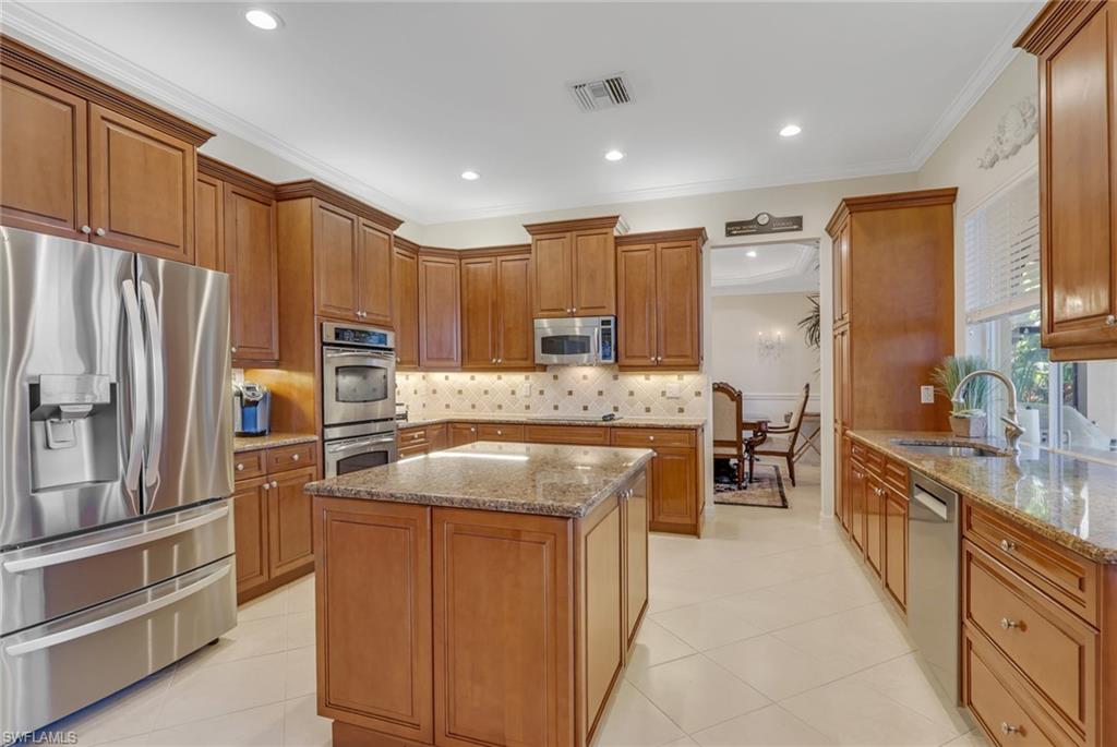 1859 Ivory Cane Point Naples, FL 34119 - Photo 14 of 50 Kitchen featuring appliances with stainless steel finishes, brown cabinetry, light stone countertops, ornamental molding, and backsplash