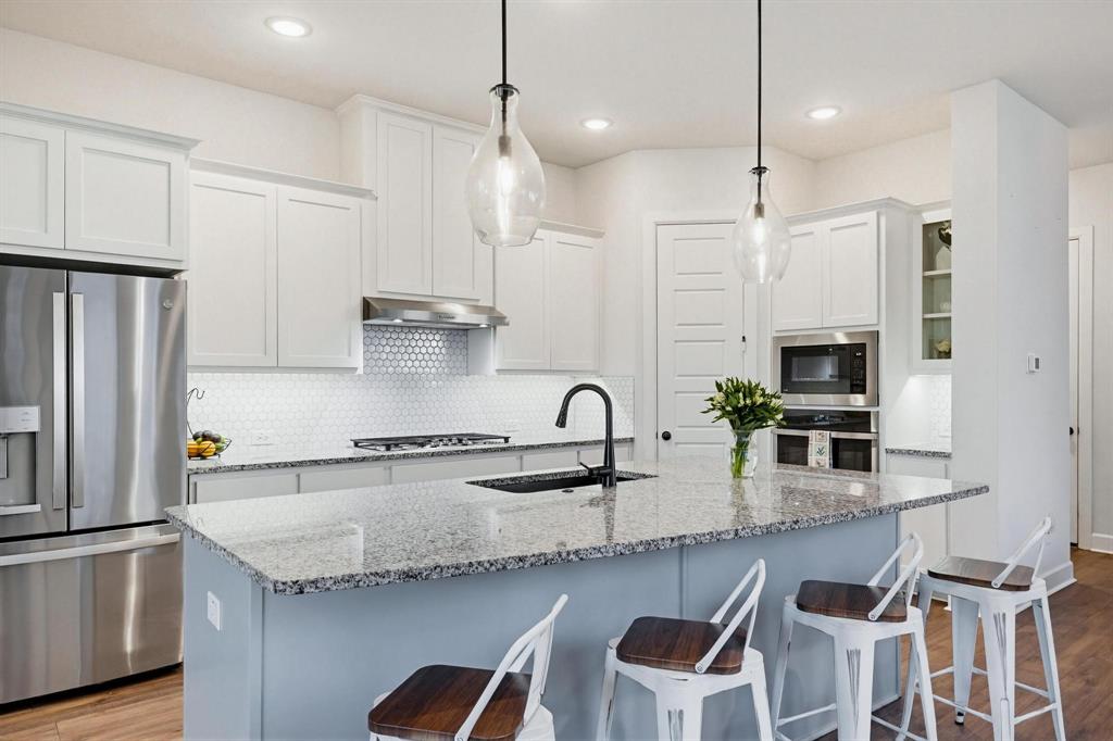 9341 Loggerhead Way Fort Worth, TX 76118 - Photo 12 of 35 Spacious kitchen featuring an expansive granite island with seating, stainless steel appliances, shaker-style cabinetry, a penny tile backsplash, and wood-finish flooring