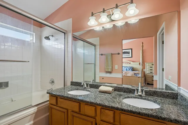 a bathroom with a granite countertop double vanity sink a mirror and shower