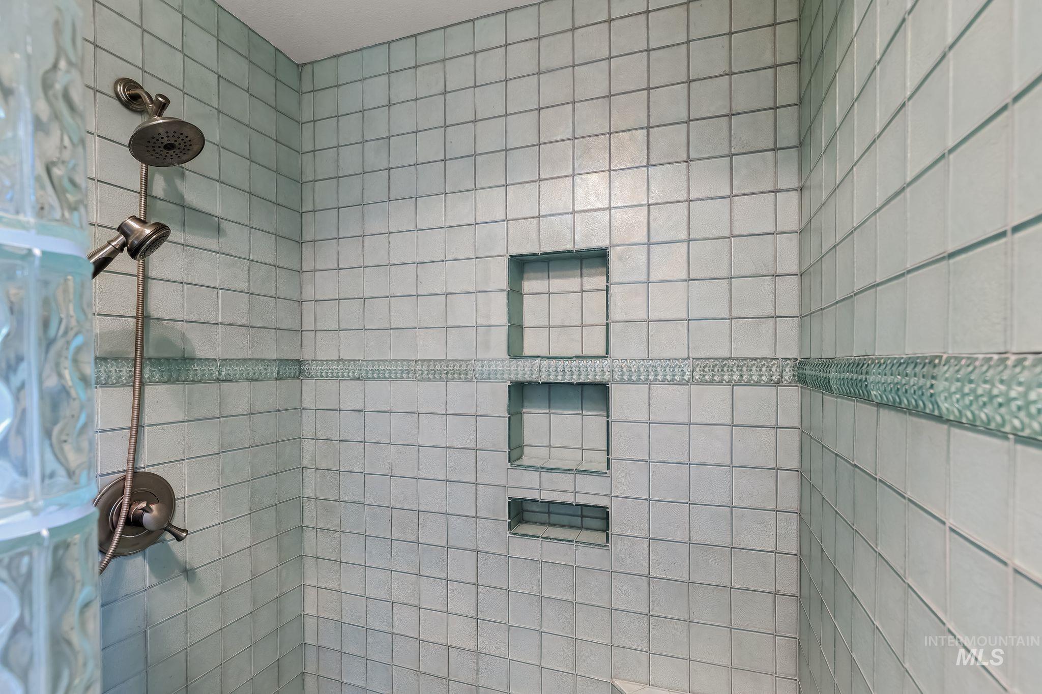 531 Silcott Road Clarkston, WA 99403 - Photo 23 of 43 Shower with light-toned square tiling, glass block wall, decorative tile band, dual shower heads, and recessed shelving