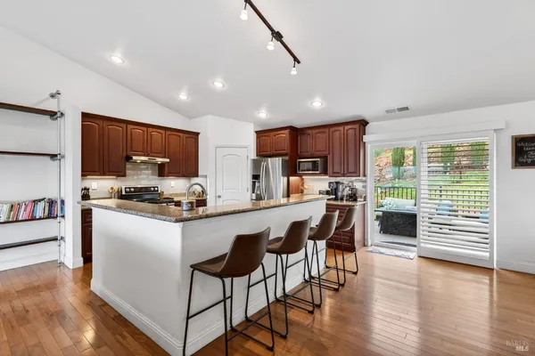 a kitchen with stainless steel appliances granite countertop wooden cabinets a refrigerator a stove a sink and a oven with wooden floor