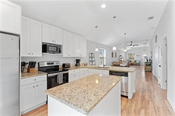 a kitchen with stainless steel appliances granite countertop a stove top oven a sink dishwasher and a refrigerator with wooden floor