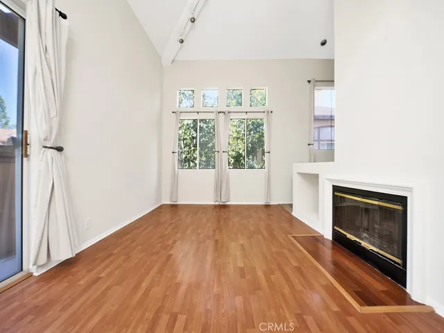 an empty room with wooden floor fireplace and windows