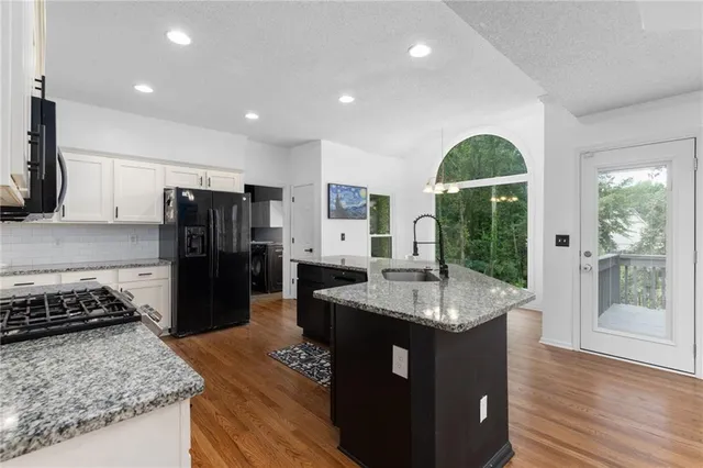 a kitchen with granite countertop kitchen island stainless steel appliances a refrigerator cabinets and wooden floor