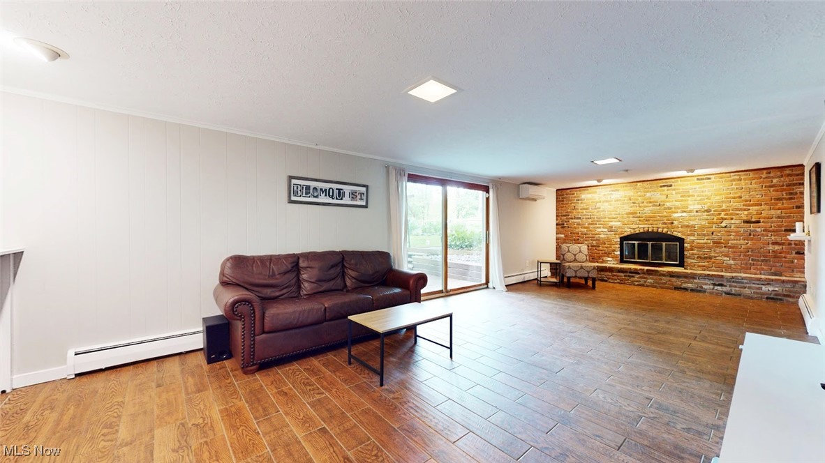 1412 Bell Road Chagrin Falls, OH 44022 - Photo 22 of 43 Family Room featuring baseboard heating, a brick fireplace, an AC wall unit, wood finished floors, and a textured ceiling