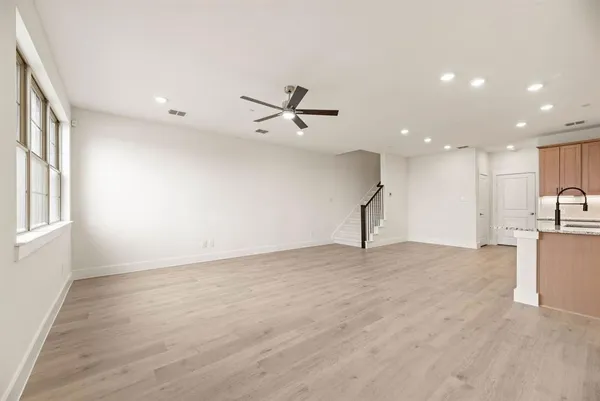 a view of a livingroom with a ceiling fan & kitchen space with wooden floor