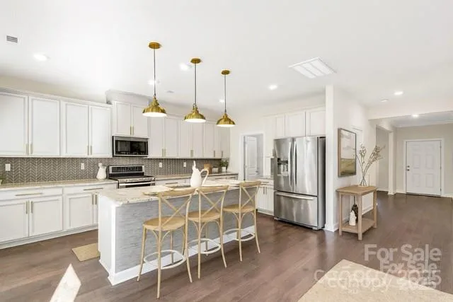 a kitchen with stainless steel appliances a refrigerator a stove a sink a dining table and chairs with wooden floor