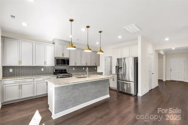 a kitchen with stainless steel appliances a refrigerator a sink dishwasher a stove and white cabinets with wooden floor