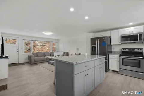 a kitchen with stainless steel appliances granite countertop a stove top oven a sink dishwasher and a refrigerator with wooden floor