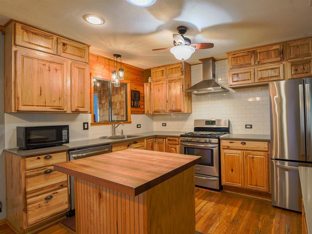 438 South Street Krum, TX 76249 - Photo 6 of 22 Kitchen featuring stainless steel appliances, decorative backsplash, decorative light fixtures, wall chimney range hood, and dark wood-style floors