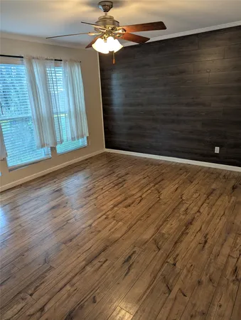 a view of an empty room with wooden floor and fan