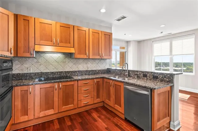 a kitchen with stainless steel appliances granite countertop wooden cabinets a sink and dishwasher with wooden floor