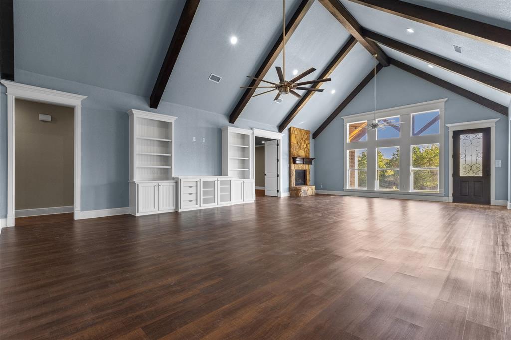 910 County Road 1111 Decatur, TX 76234 - Photo 9 of 40 Unfurnished living room featuring ceiling fan, high vaulted ceiling, beamed ceiling, a stone fireplace, and dark wood-style floors