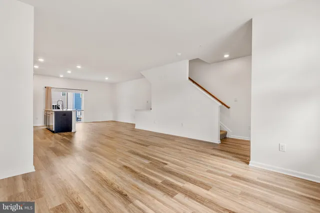 a view of empty room with wooden floor and kitchen