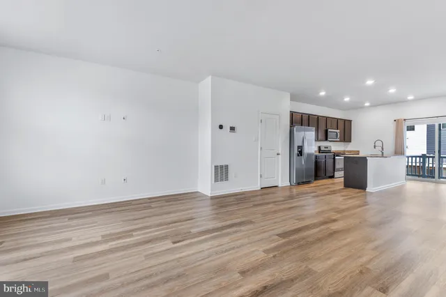 a view of an empty room with wooden floor and kitchen