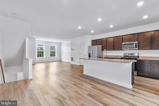 a kitchen with stainless steel appliances granite countertop a stove top oven a sink dishwasher a microwave oven and a refrigerator with wooden floor