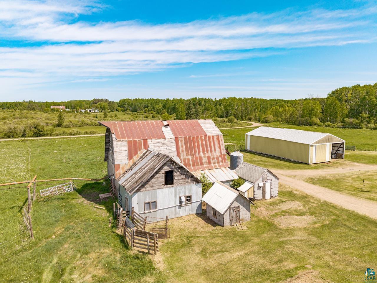 6606 Metso Road Kettle River, MN 55757 - Photo 38 of 84 Farm property featuring a large barn with a corrugated metal roof, multiple outbuildings, and a substantial detached storage building with a roll-up door