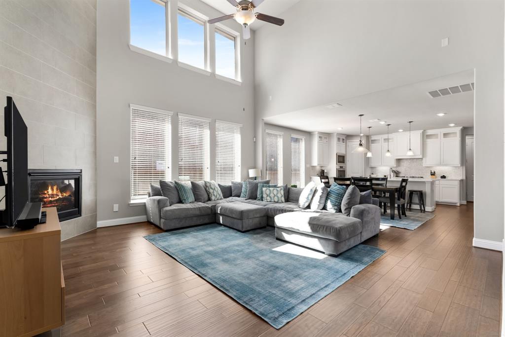 6309 Hall Road Frisco, TX 75034 - Photo 6 of 35 Living room with a tiled fireplace, dark wood-style floors, ceiling fan, and a high ceiling