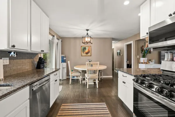a kitchen with stainless steel appliances granite countertop a stove a sink dishwasher a dining table and chairs with wooden floor