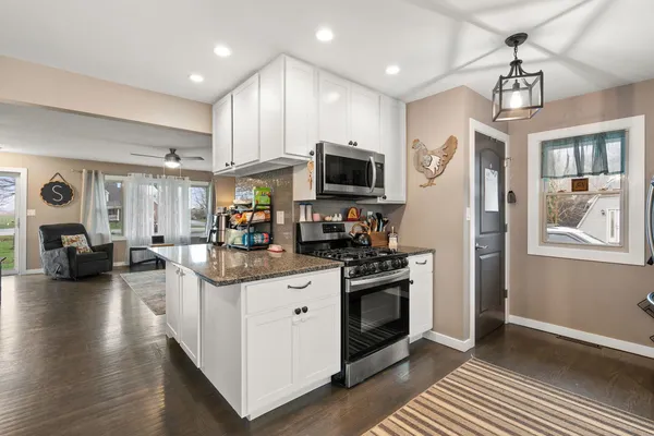 a kitchen with stainless steel appliances granite countertop a stove top oven a refrigerator a sink dishwasher and white cabinets with wooden floor
