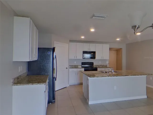 a kitchen with stainless steel appliances kitchen island granite countertop a stove a sink a refrigerator and white cabinets