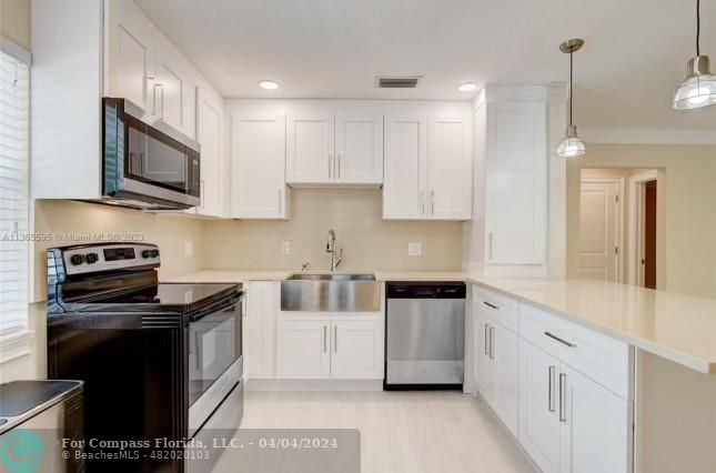 a kitchen with stainless steel appliances granite countertop grey cabinets a stove a sink and a microwave