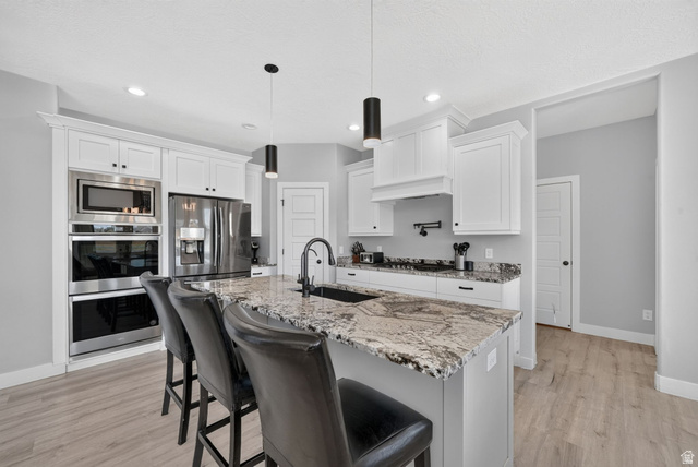 3644 Spiral Springs Road Tooele, UT 84074 - Photo 7 of 41 Modern kitchen featuring white cabinetry, light-toned wood-finish flooring, and a large island with a patterned countertop