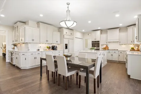 a kitchen with a dining table chairs wooden floor cabinets and appliances