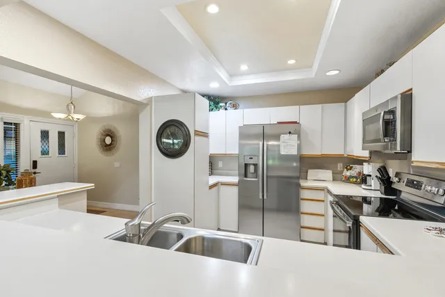 a kitchen with stainless steel appliances a refrigerator a sink a stove and white cabinets with wooden floor