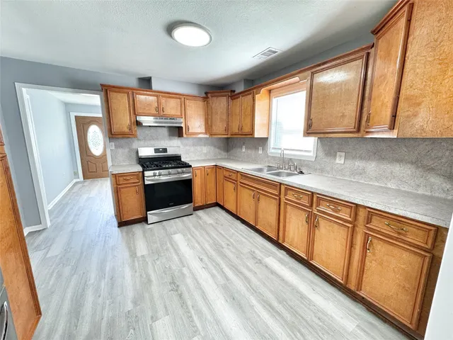 a kitchen with stainless steel appliances granite countertop wooden cabinets a refrigerator a sink a stove a microwave and wooden floors