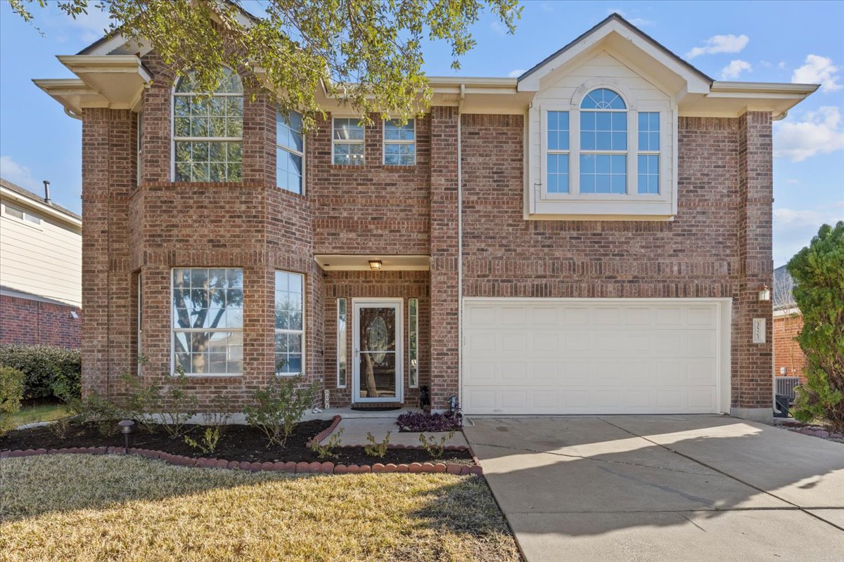 Traditional-style home featuring an attached garage, driveway, brick siding, and a front yard