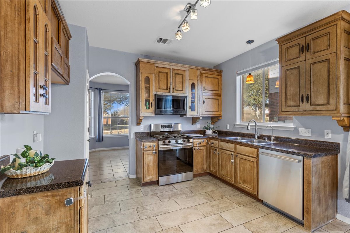 3523 Cheyenne Street Round Rock, TX 78665 - Photo 10 of 34 Kitchen featuring wood finish cabinetry, arched walkways, stainless steel appliances, decorative light fixtures, and glass insert cabinets